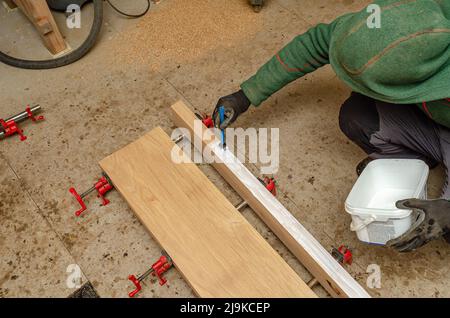 Vista dall'alto processo di verniciatura del legno. Mano con guanto con spazzola. Vernice bianca Foto Stock