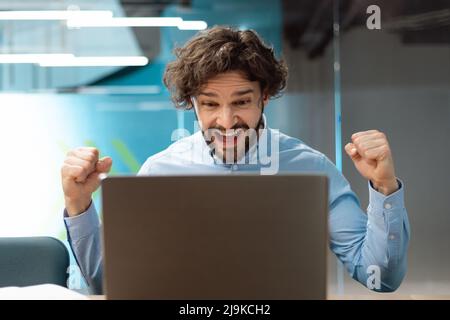Un uomo d'affari entusiasta che utilizza il pc festeggia il successo scuotendo i pugni urlando sì Foto Stock