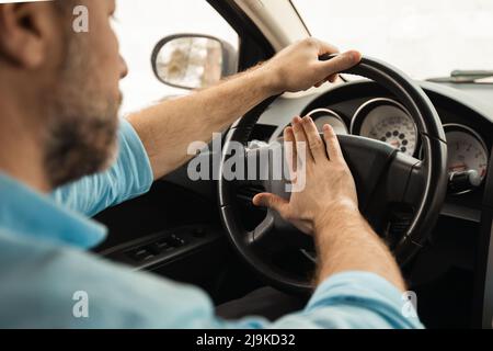 Uomo adulto che guida l'auto e la levigatura, premendo il clacson Foto Stock