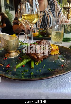 Deliziosi tournedos di lusso serviti con fagioli verdi, peperoni rosa, patate e patatine fritte in un ristorante bistro Foto Stock