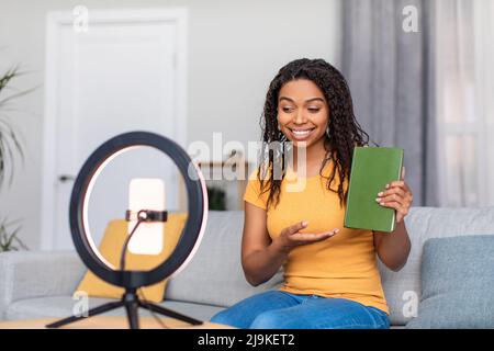 Videoblog e concetto di tecnologia. Positivo nero femmina blogger video di registrazione della recensione del libro a casa Foto Stock