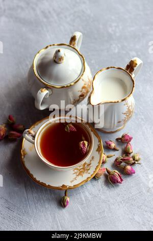 Tè con rose primo piano foto. Tè alle erbe in una piccola tazza di ceramica bianca su un tavolo. Sfondo grigio chiaro con spazio di copia. Foto Stock