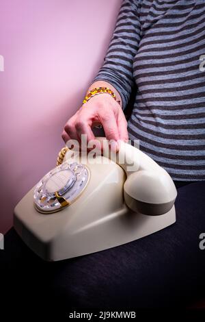 Donna con un vecchio telefono poggiato sulle gambe. Foto Stock