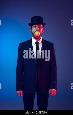 Ritratto creativo di giovane uomo elegante in abito da lavoro e cappello bowler sulla sua testa isolato su sfondo blu scuro studio. Concetto di arte, moda Foto Stock