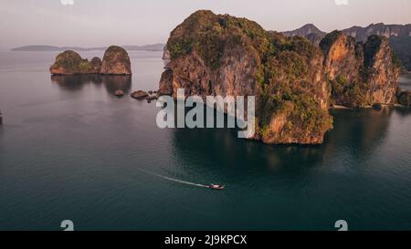 Alba a Railay Beach a Krabi Thailandia con una barca a coda lunga tailandese che passa attraverso le scogliere calcaree nel mare delle Andamane Foto Stock