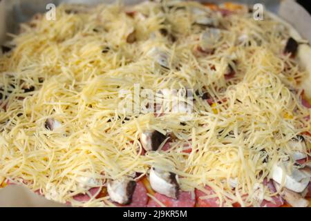 Defocalizzare il primo piano attorno alla pizza intera con mozzarella grattugiata sul tetto. Defocalizzare gli ingredienti del primo piano per la pizza sull'impasto. Pizza italiana fatta in casa Foto Stock