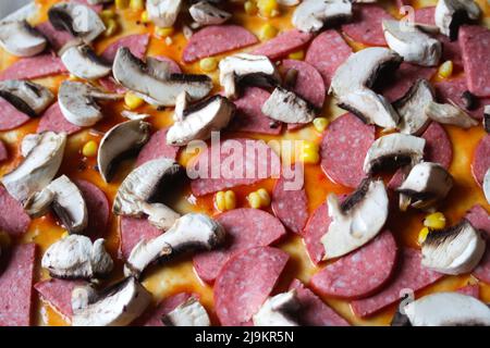 Defocalizzare gli ingredienti del primo piano per la pizza sull'impasto. Salsa di pomodoro rosso, salsicce, mais dolce. Pizza italiana fatta in casa. Home culinario. Vista dall'alto. Cuisi italiana Foto Stock