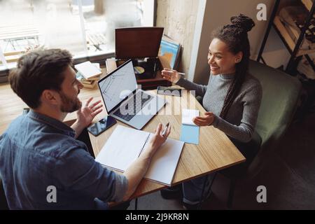 Giovani felici e misti-gare colleghi che parlano e lavorano in un bar al portatile. Concetto di brainstorming. Foto Stock