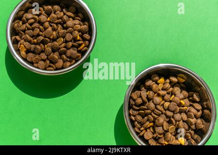 Due ciotole per animali domestici con kibble sullo sfondo verde, immagine ravvicinata Foto Stock