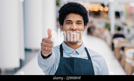 Amichevole felice africano americano maschio lavoratore cameriere venditore in grembiule uomo mostra un buon segno perfetto con mano piccolo imprenditore di caffè ristorante Foto Stock