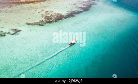 Cima aerea giù acque tropicali turchesi con una barca a coda lunga thailandese che passa davanti a una barriera corallina e l'isola di Ko Poda nel mare delle Andamane di Krabi Thailandia Foto Stock