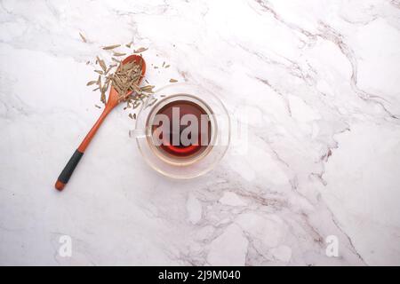 Foglie di tè secco su cucchiaio e tè verde su sfondo piastrelle Foto Stock