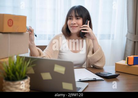 Giovane donna asiatica usando il suo telefono e lavorando a casa, piccola impresa donna proprietario o Start up imprenditore di piccola impresa che lavora on-line marketi Foto Stock