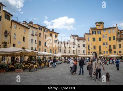 Luuca, Toscana, Italia, 08 maggio 2022 - Vista su Piazza del Anfiteatro di Luuca, con caffè, ristoranti e gente in una giornata di sole con cielo blu. Foto Stock