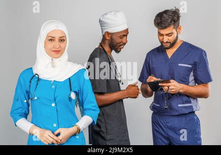 Gruppo di paramedici sorridenti su sfondo grigio. donna medico musulmana con colleghi chirurgo africano e indiano Foto Stock