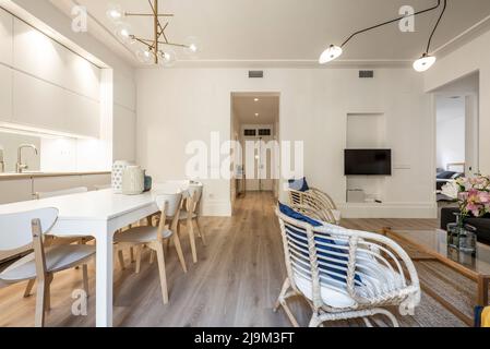 Appartamento con tavolo da pranzo in legno bianco con cucina a vista e divani in vimini Foto Stock