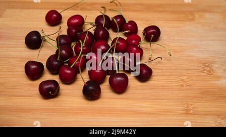 Collezione di ciliegie rosse fresche mature con gambo posto su un asse di legno. Foto Stock