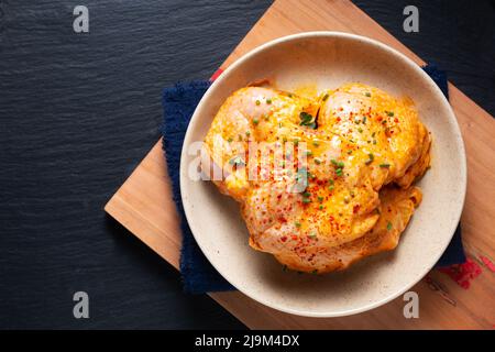 Concetto di cibo fatto in casa piccante cosce di pollo marinata in ceramica ciotola su tavola di legno con sfondo nero e spazio copia Foto Stock