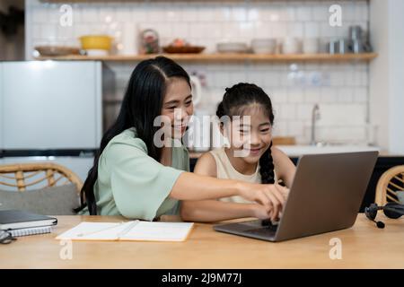 Madre che insegna ai bambini di fare i loro compiti a casa. Buona famiglia asiatica che usa il portatile insieme a casa. Giovani genitori asiatici famiglia aiutare Foto Stock