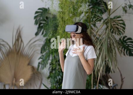 Intrattenimento virtuale nel giardino di casa. Donna gioita in visore VR che gioca a un videogioco interattivo Foto Stock