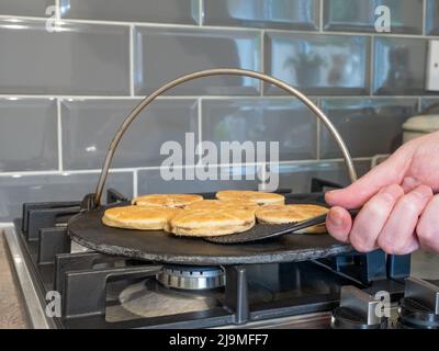 Chef che gira la torta gallese mentre cucinano su una griglia in ghisa sopra una fiamma del piano cottura a gas Foto Stock