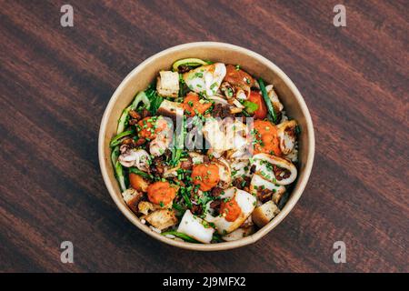 Vista dall'alto della ciotola da asporto con insalata fatta di anelli di calamari fritti e verdure con crostini e salsa sul tavolo di legno nel ristorante Foto Stock