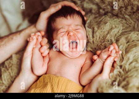 Alto angolo di giovane madre e padre irriconoscibile con capelli scuri che tengono la mano di adorabile neonato yawning sdraiato e dormire su letto morbido in da Foto Stock