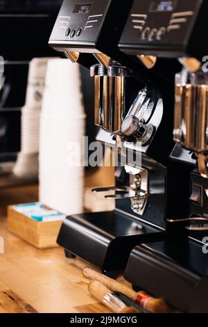 Moderne macchine per il caffe' nere con dettagli cromati poste su un banco di legno vicino a tazze di carta in un moderno cafe' Foto Stock