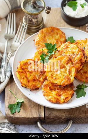 Rosolate o frittelle di patate su un piatto con prezzemolo e una ciotola di panna acida sullo sfondo Foto Stock