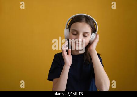 Ragazza adulata con capelli scuri in t shirt godendo la musica con occhi chiusi mentre si ascolta la canzone preferita in cuffie contro backgro giallo Foto Stock