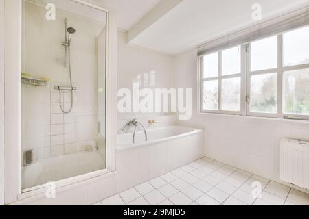 Vasca in ceramica bianca posta vicino alla doccia a parete piastrellata in un  bagno spazioso e luminoso con portasciugamani riscaldato in metallo a casa  Foto stock - Alamy