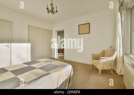 Letto confortevole con coperta posta vicino alle finestre e radiatore in camera da letto luminosa a casa Foto Stock