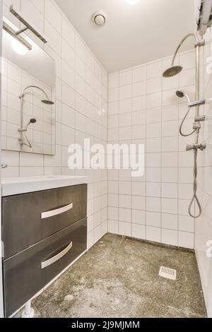 Doccia con tubo posizionato su piastrelle bianche vicino lavello sopra i cassetti a parete con specchio nella stanza da bagno elegante e luminosa a casa Foto Stock