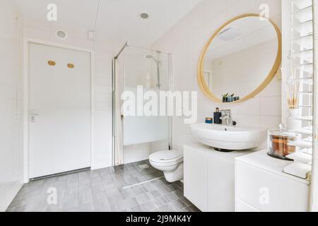 Interno di ampio bagno con wc in ceramica bianca vicino cabina doccia con porta di vetro e lavandino Foto Stock