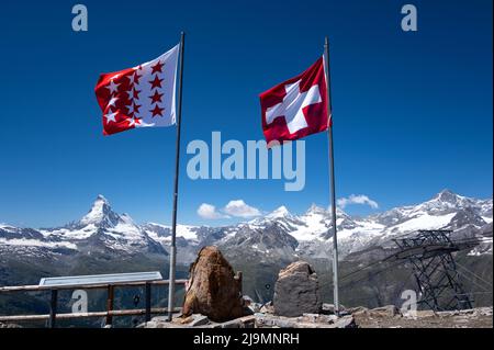 Vista della bandiera svizzera in cima alla cima del Rothorn con la splendida cima del ghiacciaio del Cervino sullo sfondo. Popolare Sunrise Spot a Zermatt Foto Stock