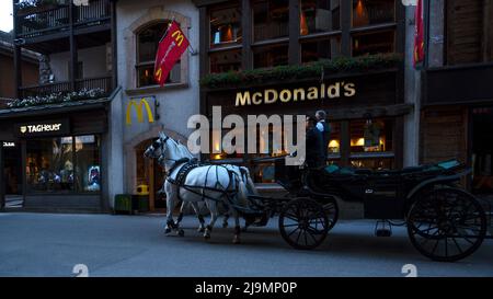 Pullman a cavallo che trasporta i turisti sulla strada principale dello shopping di Zermatt, un villaggio ecologico senza auto circondato da ristoranti e negozi Foto Stock