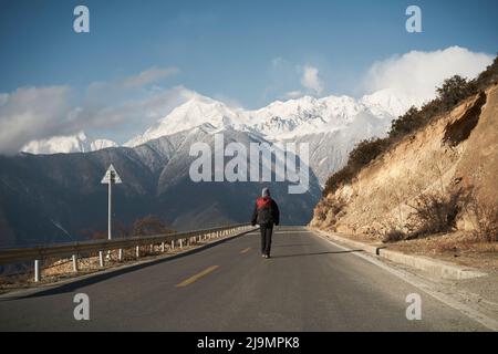 vista posteriore di un escursionista asiatico con zaino a piedi in autostrada con montagna di meili innevata sullo sfondo Foto Stock