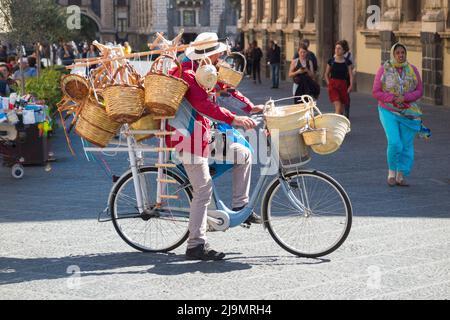 Uomo medio/anziano, siciliano locale, uomo bric-a-brac mobile in bicicletta che vende cesti di vimini tessuti ai turisti, dalla sua bicicletta, in Piazza del Duomo, Catania, Sicilia. Italia (129) Foto Stock