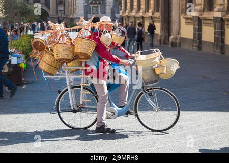 Uomo medio/anziano, siciliano locale, uomo bric-a-brac mobile in bicicletta che vende cesti di vimini tessuti ai turisti, dalla sua bicicletta, in Piazza del Duomo, Catania, Sicilia. Italia (129) Foto Stock