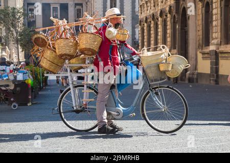 Uomo medio/anziano, siciliano locale, uomo bric-a-brac mobile in bicicletta che vende cesti di vimini tessuti ai turisti, dalla sua bicicletta, in Piazza del Duomo, Catania, Sicilia. Italia (129) Foto Stock