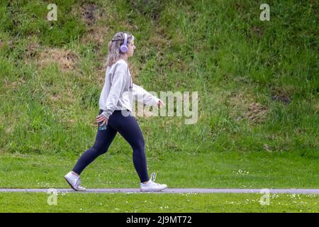 Giovane donna attraente che prende l'esercitazione che indossa le cuffie e che trasporta il telefono mobile a Warminster, Wiltshire, Regno Unito il 24 maggio 2022 Foto Stock