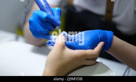 Manicurista utilizza la macchina elettrica per manicure per rimuovere lo smalto per unghie dalle mani nel salone delle unghie Foto Stock