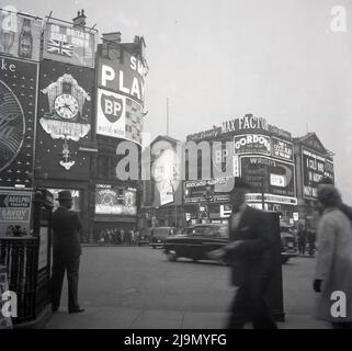 1961, storico, uomo in un cappello in piedi da ringhiere a Piccadilly circus, Londra, Inghilterra, Regno Unito, con i famosi cartelloni al neon che mostrano gli inserzionisti e le marche del giorno, tra cui i giocatori sigarette, Bristol Tiped sigarette, BP, Gordons Gin, Fattore max e ridiffusione associata. Il musical di Meredith Willson, The Music Man è al Teatro Adelphi nel West End. Foto Stock