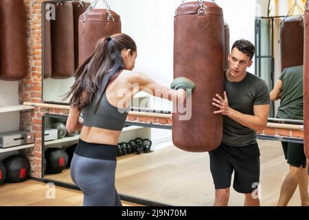 Atletica femminile in sacco di pugilato Mittens mentre facendo esercizio con l'aiuto di allenatore personale maschile nel moderno fitness club Foto Stock