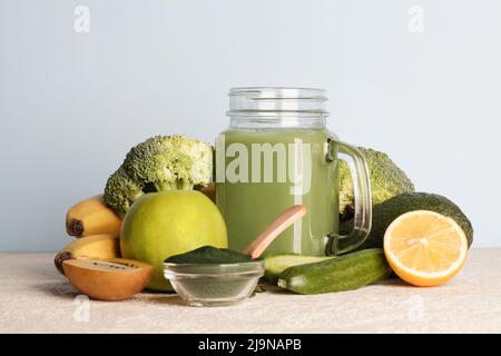 frullato verde in bottiglia di vetro, polvere di spirulina, verdure e frutta su sfondo blu. dieta vegana sana, cruda. spazio copia Foto Stock