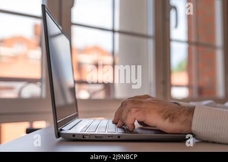 Uomo che lavora su un computer portatile in casa con grandi finestre di luce. Foto Stock