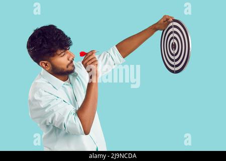Vista laterale del giovane uomo indiano che tiene il bersaglio e punta la freccia piccola a Bullseye Foto Stock