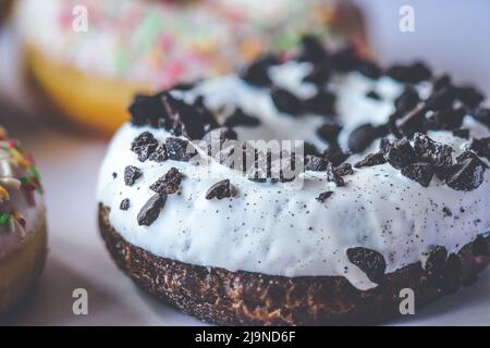 Primo piano di ciambella ad anello con glassa bianca cosparso di biscotti neri Foto Stock