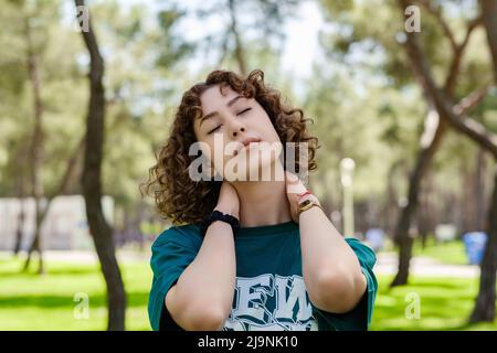 Bella donna rossa che indossa una maglietta verde in piedi sul parco cittadino, all'aperto godersi aria fresca all'aperto, rilassarsi con gli occhi chiusi, sentirsi vivi, BREA Foto Stock