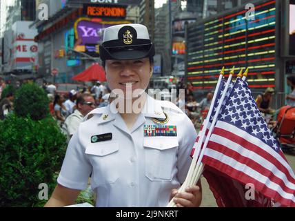 CTIC Park, una donna della Marina con diverse medaglie, si pone con una manciata di bandiere americane in un evento di reclutamento. A Times Square, New York City. Foto Stock